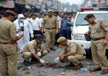 मेरठ की सड़क पर फायरिंग के बाद जांच करती पुलिस और जुटी भीड़ का दृश्य।