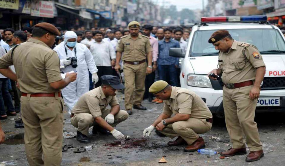 मेरठ की सड़क पर फायरिंग के बाद जांच करती पुलिस और जुटी भीड़ का दृश्य।