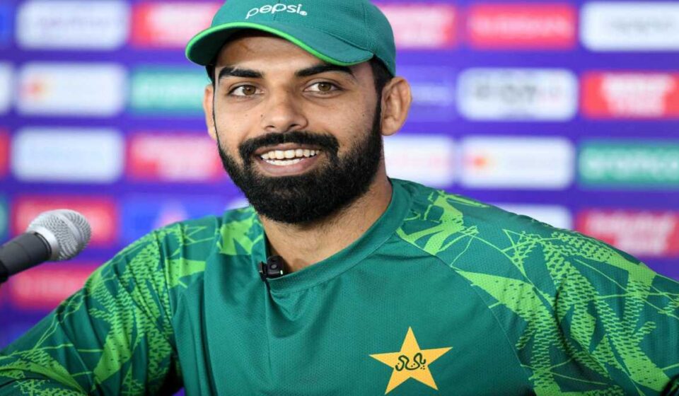 शादाब खान प्रेस कॉन्फ्रेंस में मीडिया से बातचीत करते हुए, साथ में PCB का लोगो और पाकिस्तान टीम की झलक।