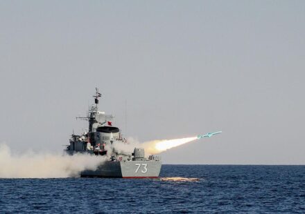 अमेरिकी एयरक्राफ्ट कैरियर, ईरानी मिसाइल अभ्यास और होरमुज स्ट्रेट से गुजरते तेल टैंकर की प्रतीकात्मक तस्वीर।