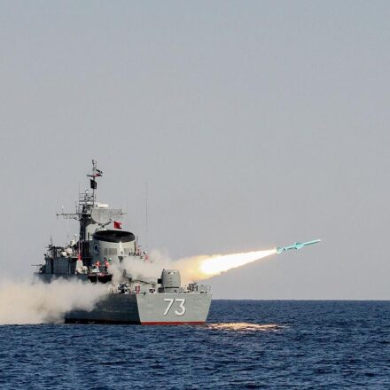 अमेरिकी एयरक्राफ्ट कैरियर, ईरानी मिसाइल अभ्यास और होरमुज स्ट्रेट से गुजरते तेल टैंकर की प्रतीकात्मक तस्वीर।