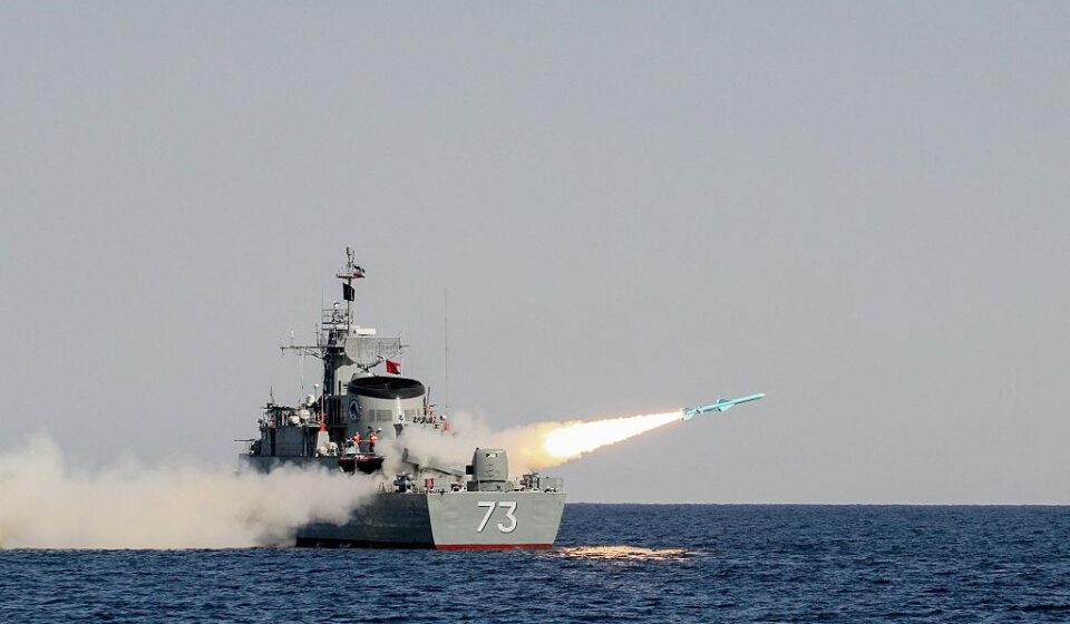 अमेरिकी एयरक्राफ्ट कैरियर, ईरानी मिसाइल अभ्यास और होरमुज स्ट्रेट से गुजरते तेल टैंकर की प्रतीकात्मक तस्वीर।