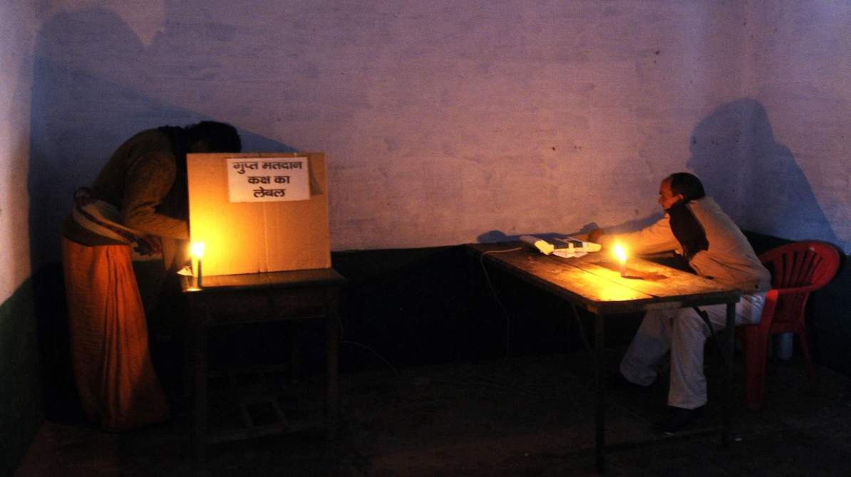 एक भारतीय मतदान केंद्र जहां बिजली की कमी के कारण अंधेरा है और अधिकारी निरीक्षण कर रहे हैं।